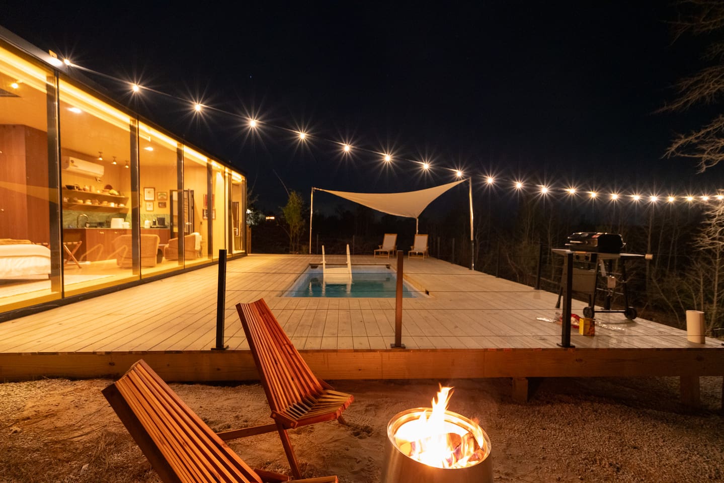 Mirror House at dusk — mirror-clad cabin with deck pool and string lights